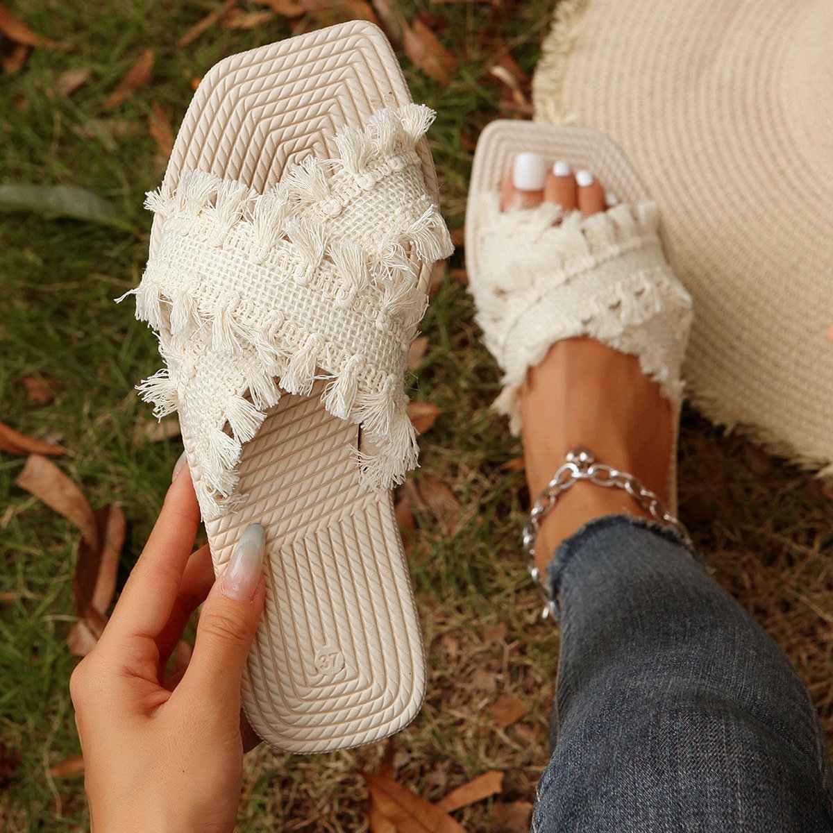 Sandali estivi intrecciati bianchi con frange, indossati su prato verde. Scarpe donna casual, moda estiva, comfort, stile boho chic.