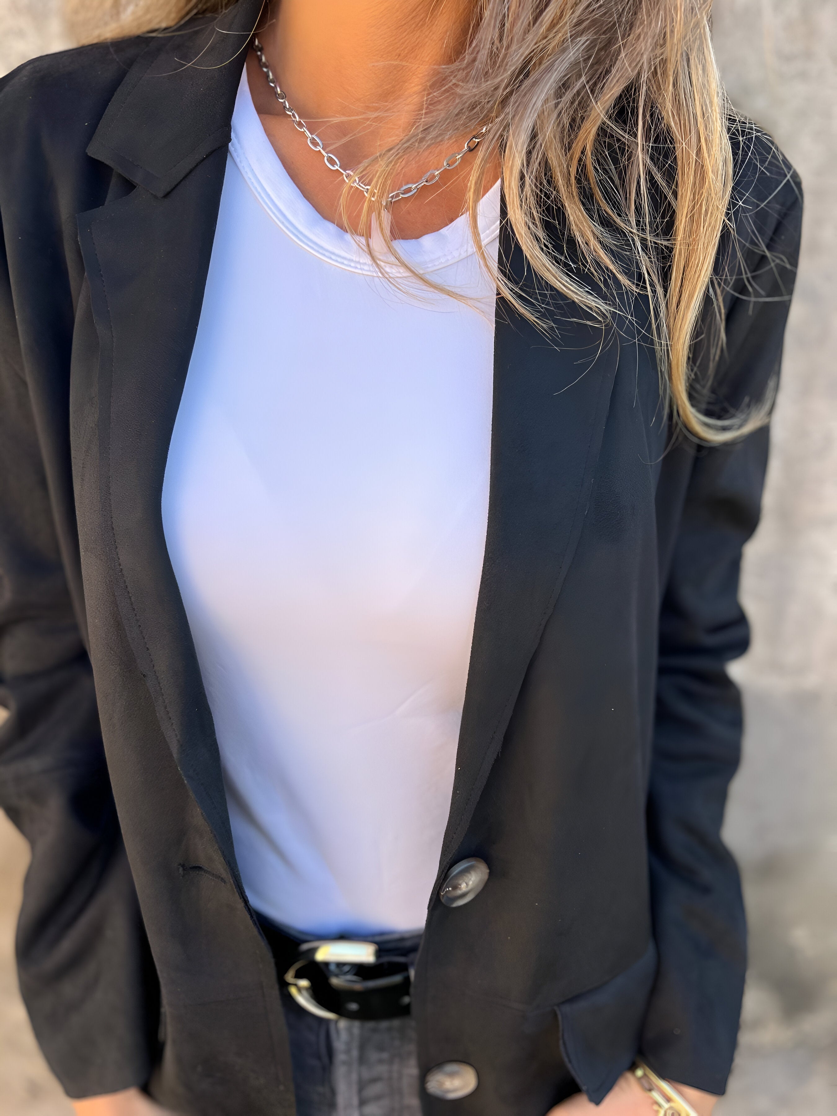 Donna con giacca nera elegante, maglietta bianca e collana d'argento. Moda femminile, abbigliamento casual chic, stile contemporaneo.