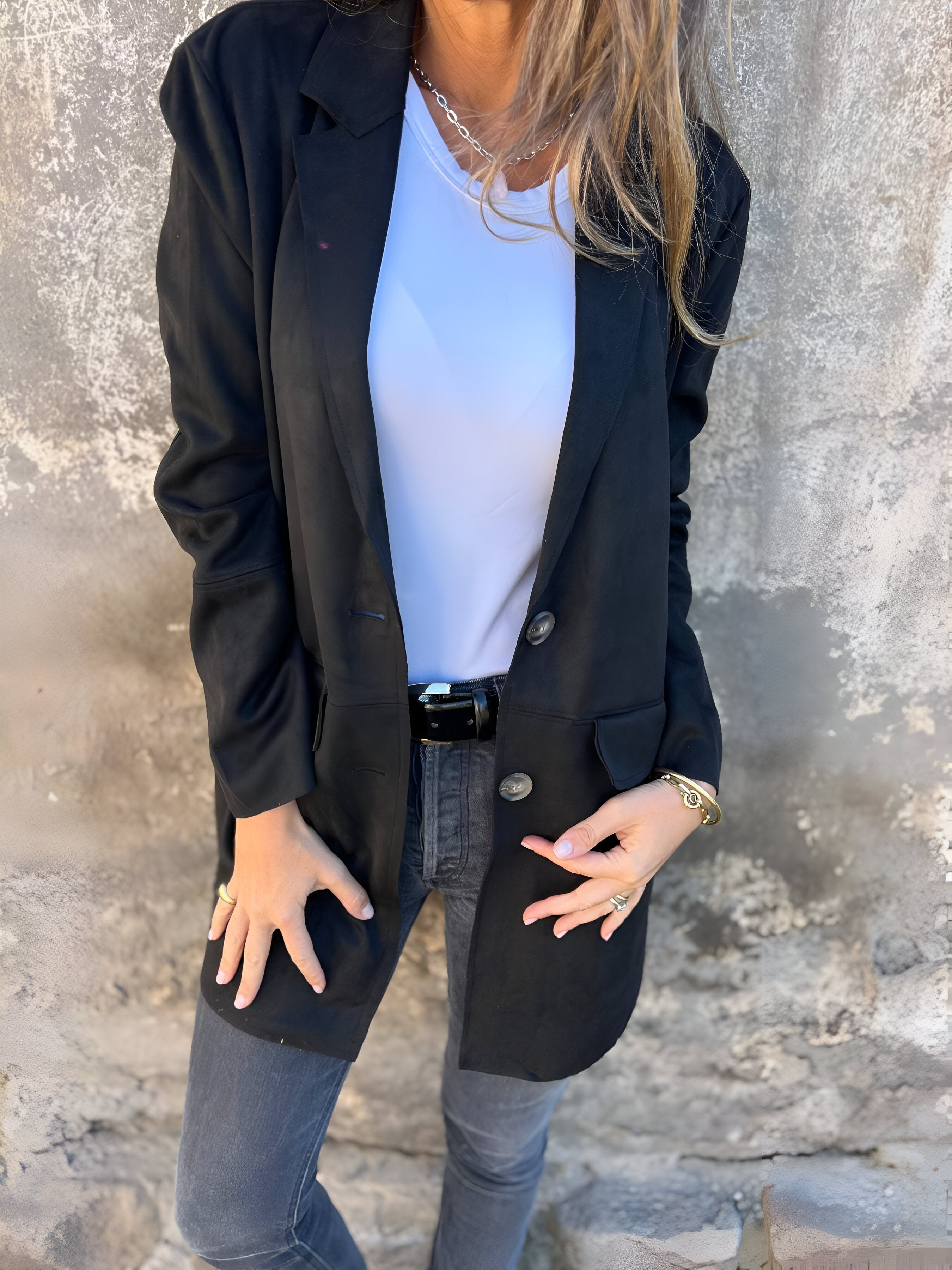 Donna con giacca nera elegante, maglietta bianca e jeans grigi. Moda casual chic, abbigliamento autunnale, stile urbano femminile.