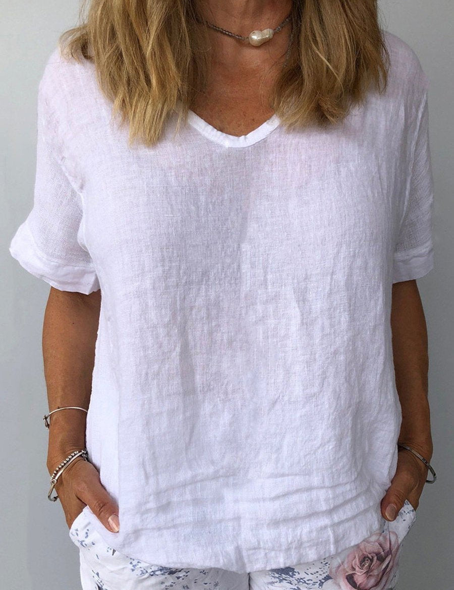 Donna con maglietta bianca in lino, scollo a V, maniche corte. Stile casual estivo, moda femminile, abbigliamento leggero e traspirante.