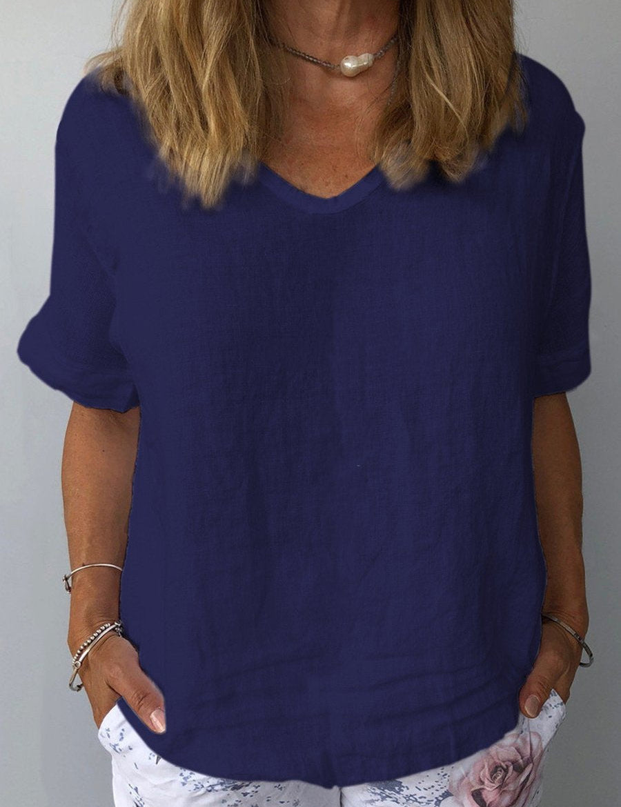 Donna con maglietta blu scuro in lino, scollo a V, maniche corte, abbinata a pantaloni bianchi con stampa floreale. Moda estiva casual elegante.