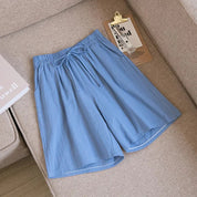Pantaloncini estivi da uomo in cotone azzurro, con elastico in vita e laccio, su divano beige. Design casual e comodo per la stagione calda.