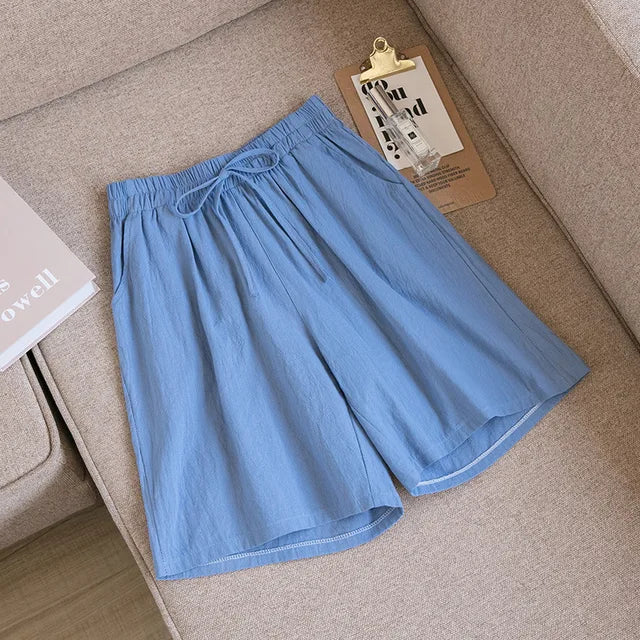 Pantaloncini estivi da uomo in cotone azzurro, con elastico in vita e laccio, su divano beige. Design casual e comodo per la stagione calda.