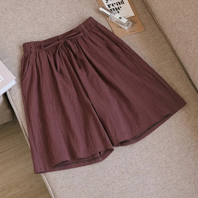Pantaloncini estivi marroni in cotone, elastico in vita, stile casual, adagiati su divano beige. Ideali per moda uomo e comfort quotidiano.