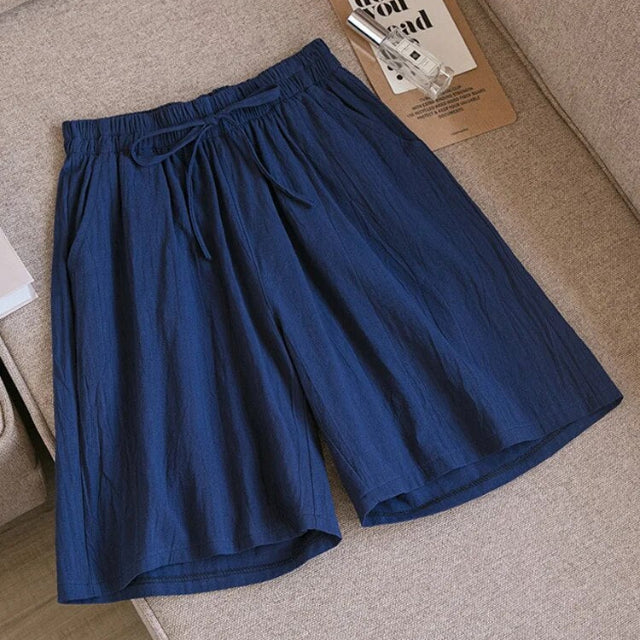 Pantaloncini blu in cotone, stile casual, con elastico in vita e laccio, su divano beige. Ideali per l'estate e il tempo libero.