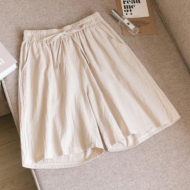 Pantaloncini beige in cotone, stile casual, con elastico in vita e tasche laterali, su divano beige. Ideali per moda estiva e comfort quotidiano.