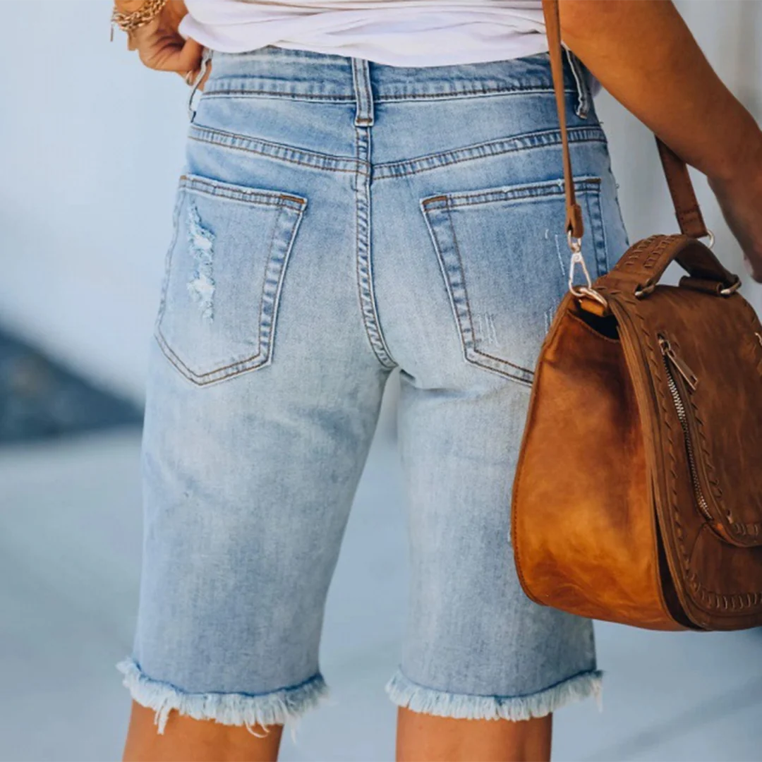 Shorts di jeans da donna con orlo sfrangiato, tasche posteriori, abbinati a borsa in pelle marrone. Moda casual estiva, abbigliamento femminile.