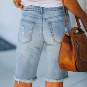 Shorts di jeans da donna con orlo sfrangiato, tasche posteriori, abbinati a borsa in pelle marrone. Moda casual estiva, abbigliamento femminile.