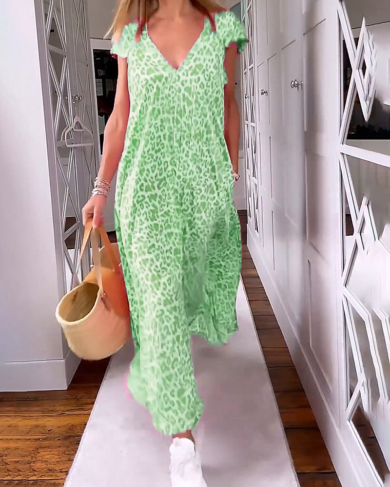 Vestito lungo verde leopardato, donna in movimento su tappeto bianco, borsa a secchiello beige, pavimento in legno, corridoio moderno.