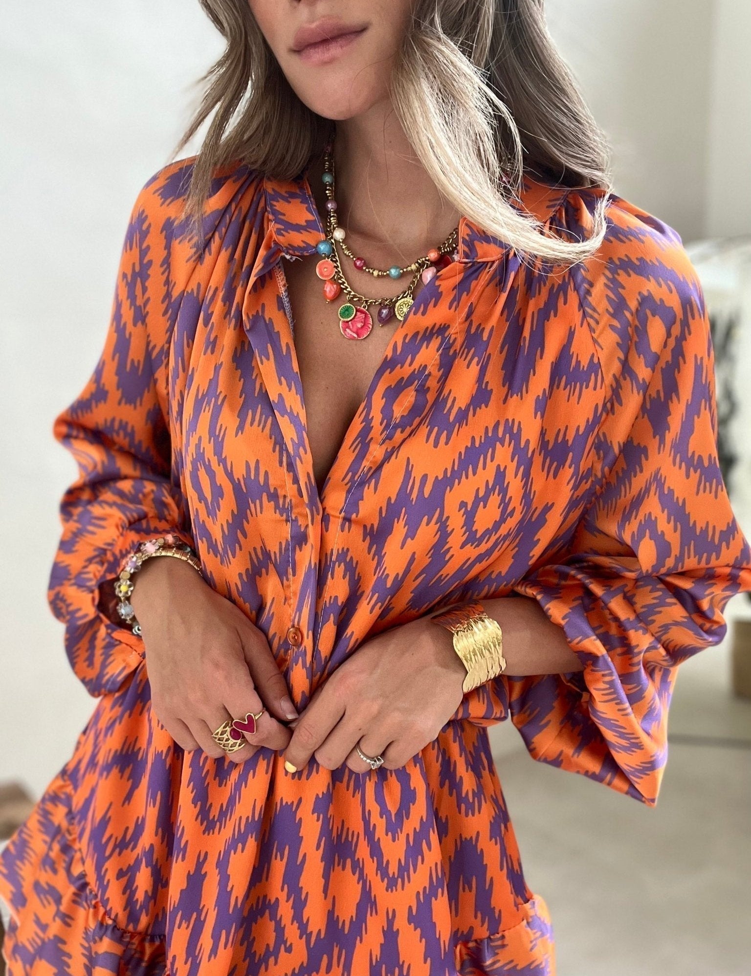 Abito donna arancione e viola con motivo ikat, collana e anelli colorati. Moda femminile, abbigliamento estivo elegante, accessori gioiello.
