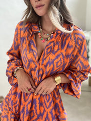 Abito donna arancione e viola con motivo ikat, collana e anelli colorati. Moda femminile, abbigliamento estivo elegante, accessori gioiello.