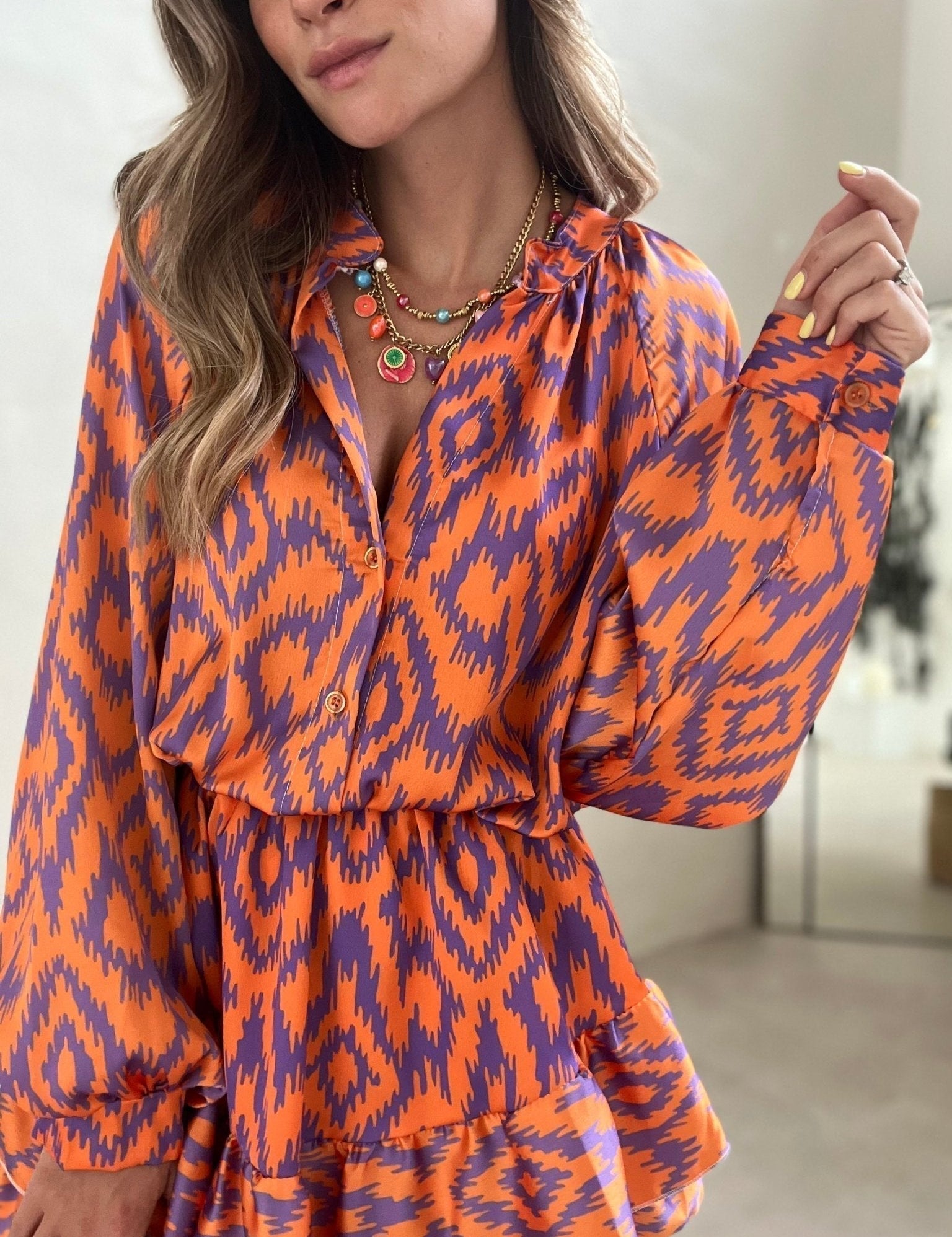 Abito donna arancione e viola con motivo ikat, maniche lunghe, collana multicolore. Moda femminile, abbigliamento elegante, tendenze 2023.
