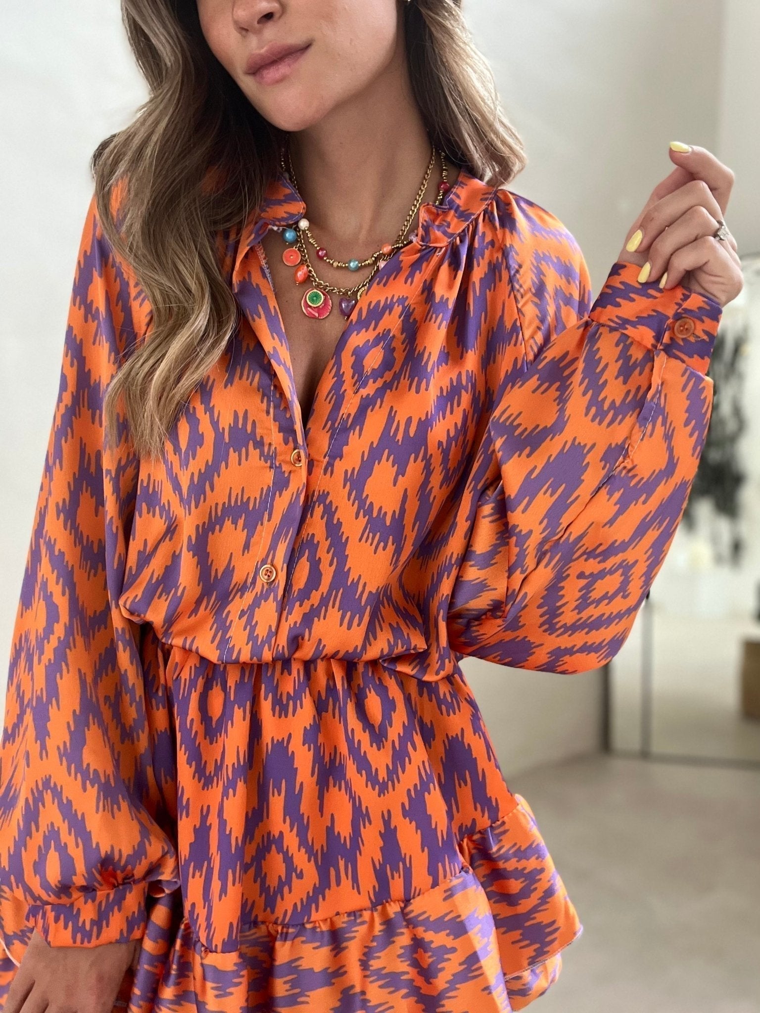 Abito donna arancione e viola con motivo ikat, maniche lunghe, collana multicolore. Moda femminile, abbigliamento elegante, tendenze 2023.