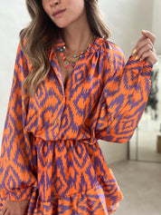 Abito donna arancione e viola con motivo ikat, maniche lunghe, collana multicolore. Moda femminile, abbigliamento elegante, tendenze 2023.
