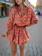 Abito corto donna arancione e blu con motivo geometrico, maniche lunghe, scollo a V, strada cittadina. Moda femminile, abbigliamento estivo elegante.
