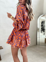 Abito corto arancione e viola con motivo geometrico, maniche lunghe e volant. Moda donna, stile casual chic, perfetto per l'estate.