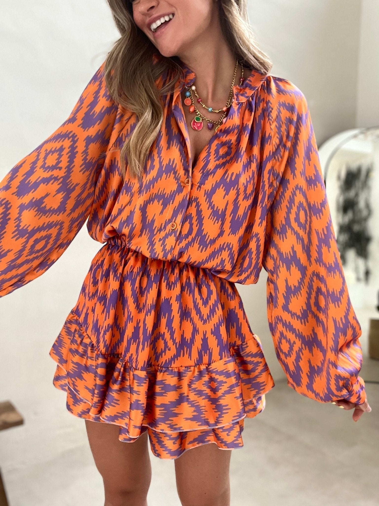Abito donna a fantasia geometrica arancione e viola, maniche lunghe, gonna a balze. Moda femminile, abbigliamento estivo elegante.