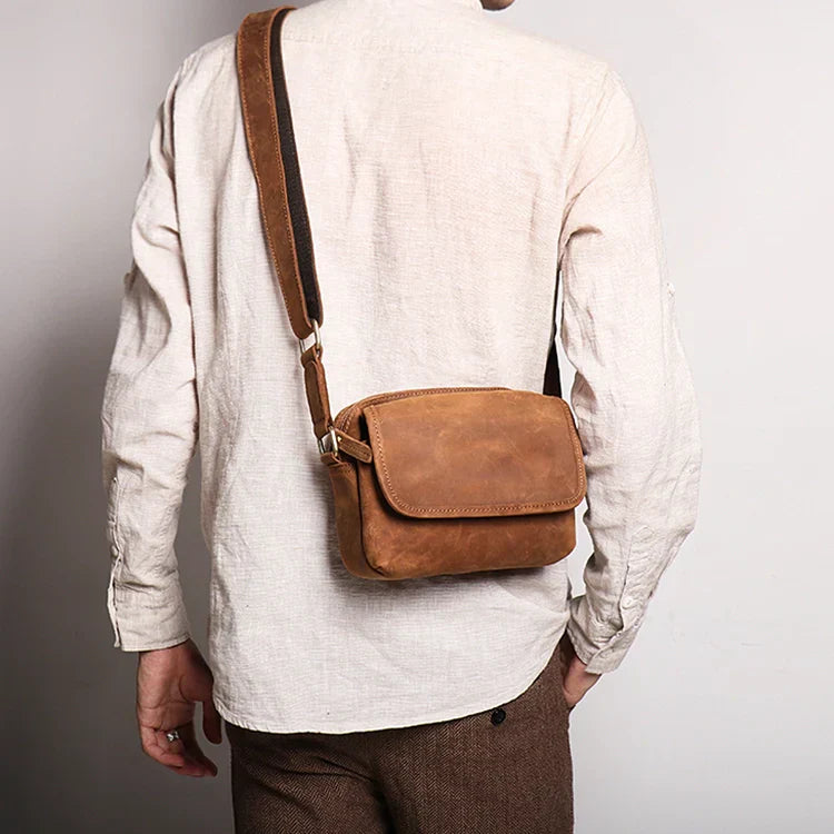 Uomo con borsa a tracolla in pelle marrone, stile vintage. Accessorio moda maschile, ideale per uso quotidiano. Elegante e pratico.