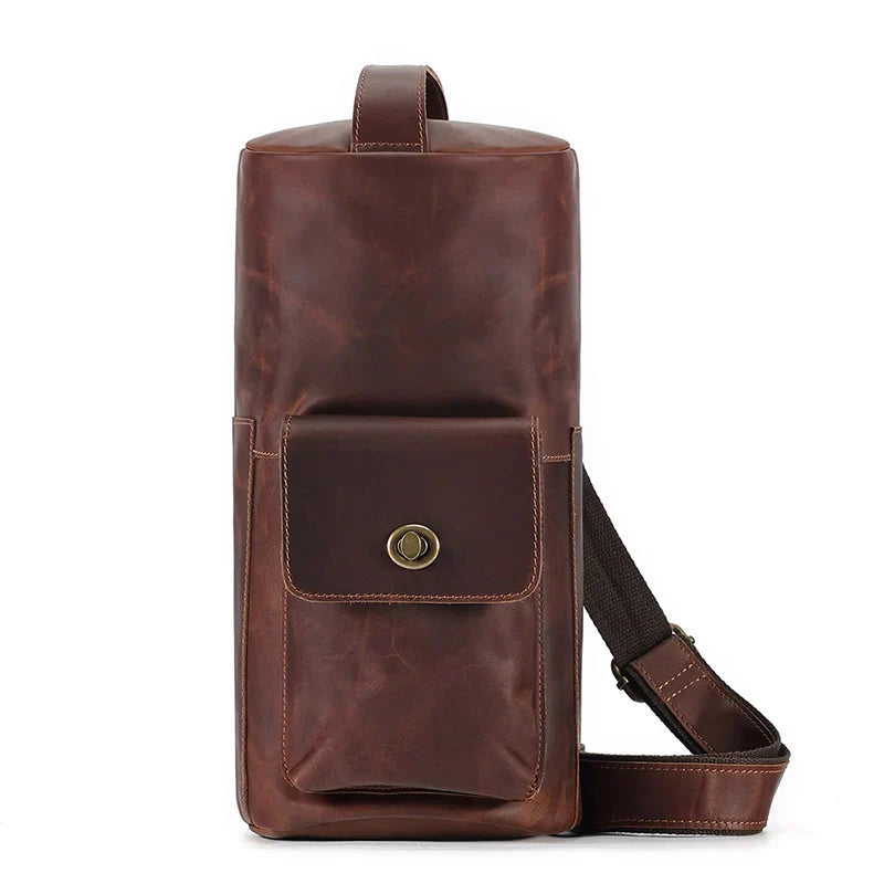 Zaino monospalla in pelle marrone, design elegante e compatto, con tasca frontale e chiusura a bottone. Ideale per viaggi e uso quotidiano.