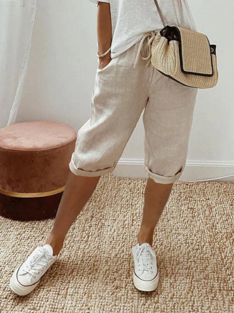 Pantaloncini beige in lino, stile casual, abbinati a sneakers bianche e borsa a tracolla intrecciata. Outfit estivo donna, moda comoda.