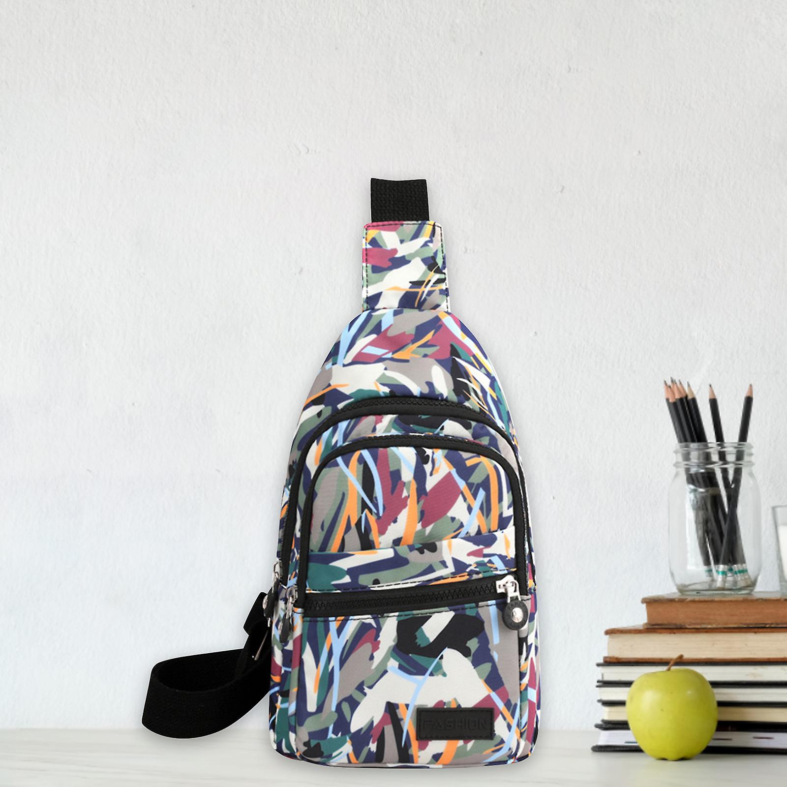 Zaino a tracolla multicolore con motivo astratto su sfondo bianco, accanto a libri, matite e mela verde. Accessorio moda casual e pratico.