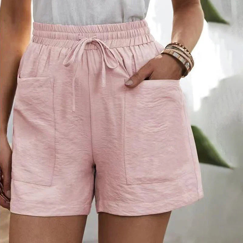 Shorts rosa da donna con tasche, elastico in vita e laccio, indossati con top bianco. Stile casual estivo, moda femminile, abbigliamento comodo.