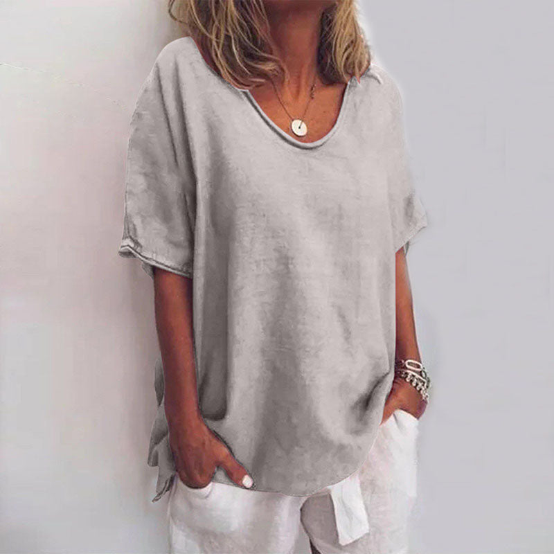 Maglietta donna grigia casual, maniche corte, scollo rotondo, tessuto leggero, abbinata a pantaloni bianchi. Look estivo elegante e confortevole.