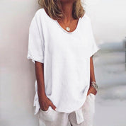 Maglietta bianca da donna, maniche corte, scollo rotondo, stile casual estivo, tessuto leggero, abbinata a pantaloni bianchi.