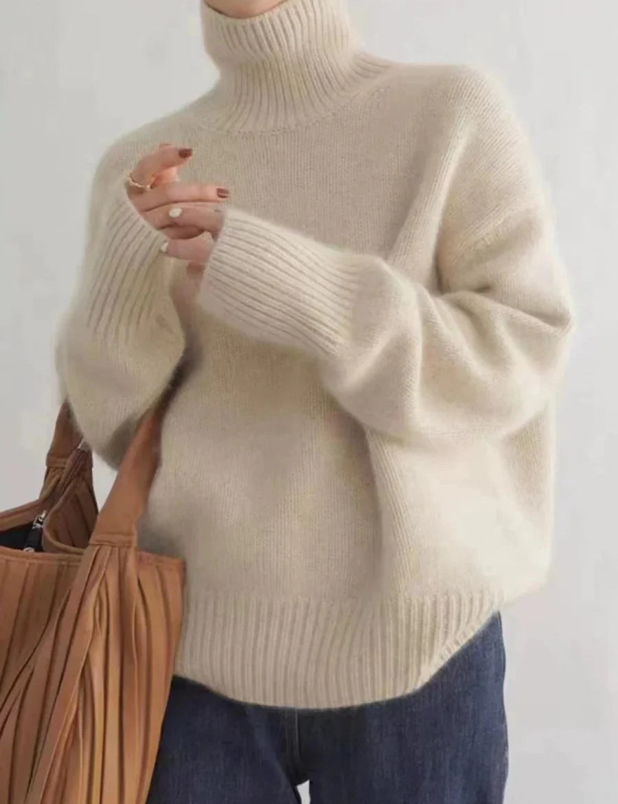 Maglione donna in lana beige a collo alto, maniche lunghe, abbinato a jeans blu. Look casual autunnale. Accessorio: borsa marrone.