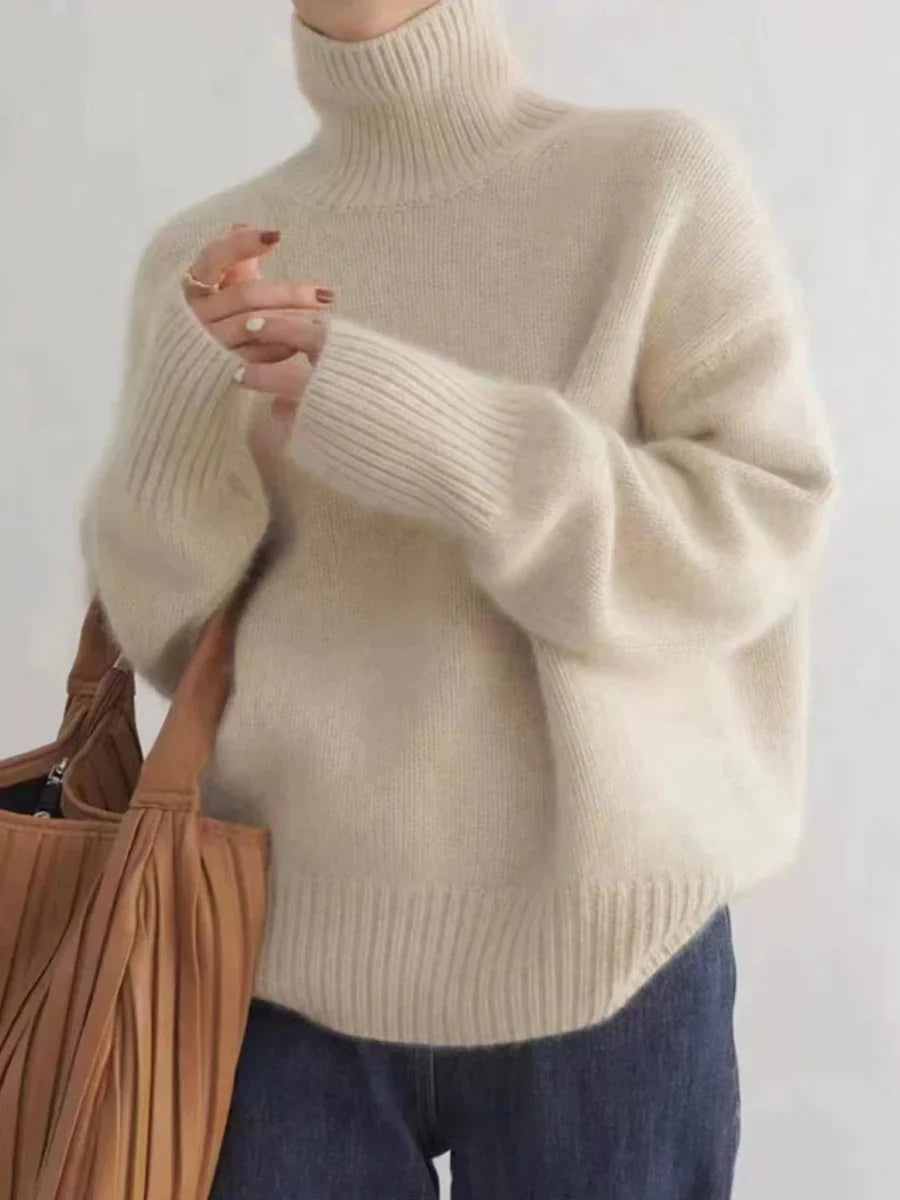 Maglione donna in lana beige a collo alto, maniche lunghe, abbinato a jeans blu. Look casual autunnale. Accessorio: borsa marrone.