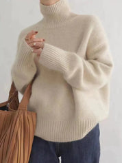 Maglione donna in lana beige a collo alto, maniche lunghe, abbinato a jeans blu. Look casual autunnale. Accessorio: borsa marrone.