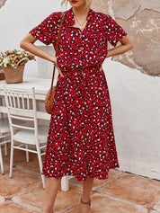 Abito rosso a fantasia leopardata, maniche corte, lunghezza media, indossato da donna. Sfondo con tavolo bianco e cesto di fiori.