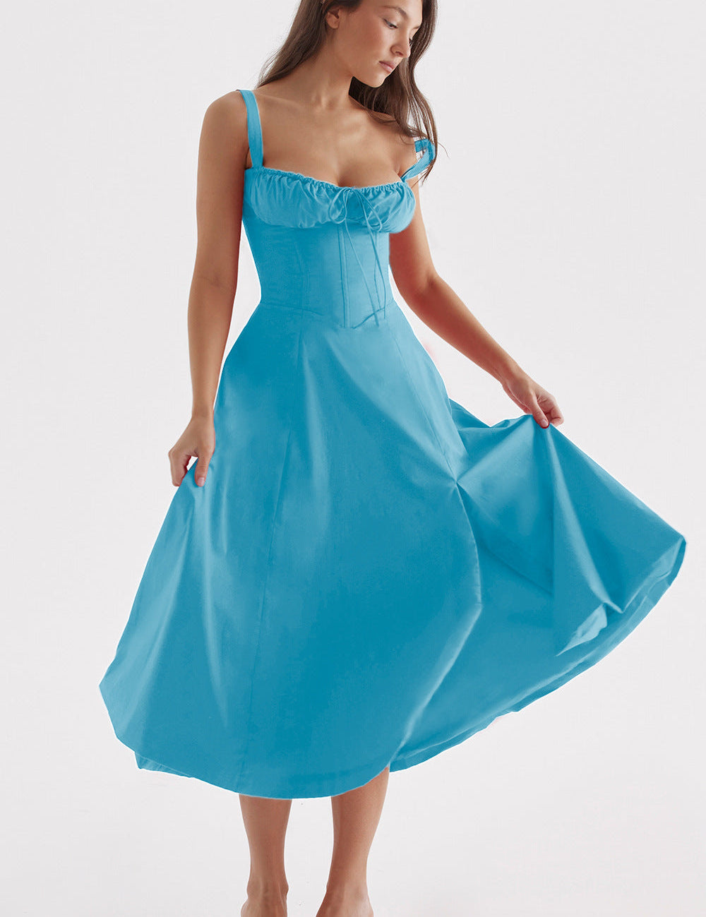 Donna in abito midi azzurro elegante, con spalline e scollo a cuore, posa su sfondo bianco. Moda femminile, abbigliamento estivo, stile chic.