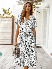 Donna con abito estivo bianco a pois neri, maniche corte, cintura in vita, borsa beige. Moda femminile, abbigliamento casual elegante.
