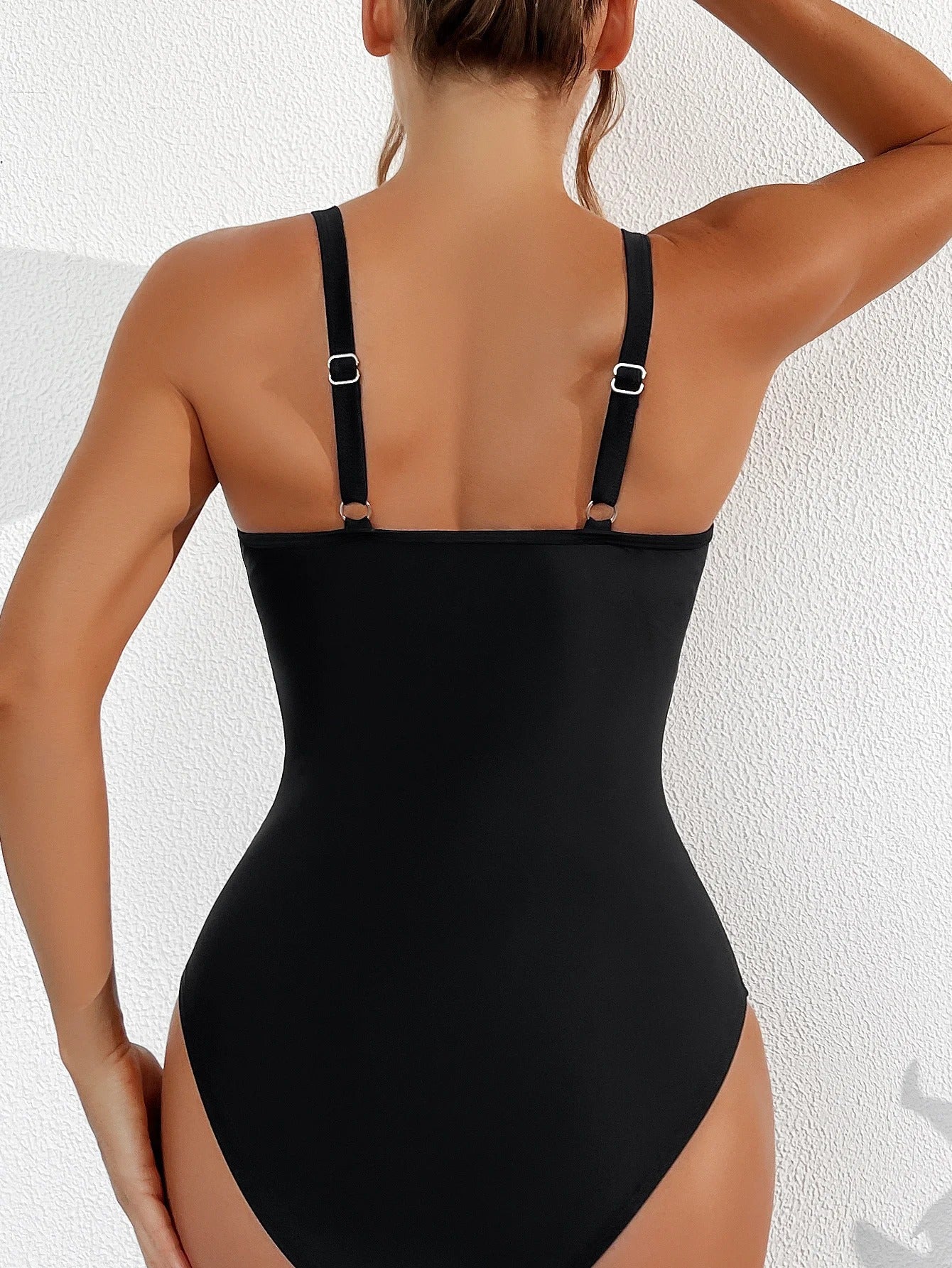 Donna in costume intero nero, spalline regolabili, vista posteriore. Moda mare, abbigliamento estivo, costume da bagno elegante.