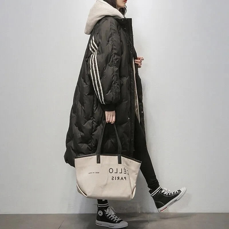 Donna con cappotto lungo nero trapuntato, cappuccio beige, borsa a mano beige "Bello Paris", scarpe Converse nere. Moda invernale casual.