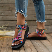 Sandali estivi donna con cinturini multicolore, suola nera, indossati con jeans strappati e perle. Scarpe moda casual, comode e trendy.