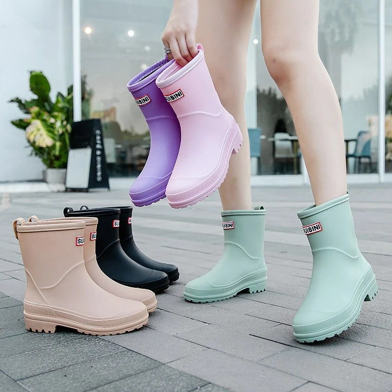 Stivali da pioggia colorati per donna su pavimento esterno. Disponibili in rosa, viola, nero, beige e verde menta. Scarpe impermeabili moda.