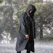 Uomo con impermeabile nero con cappuccio sotto la pioggia in una foresta. Abbigliamento antipioggia, moda outdoor, protezione impermeabile.