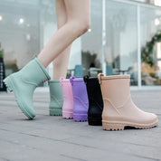 Stivali da pioggia colorati per donna su marciapiede, disponibili in verde, rosa, viola, nero e beige. Calzature impermeabili moda autunno.