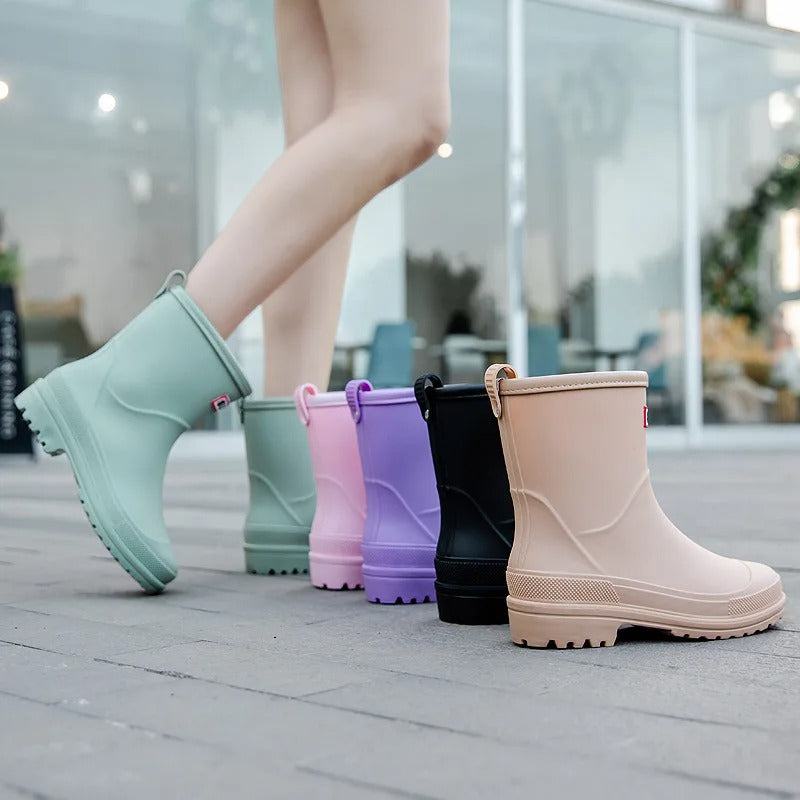 Stivali da pioggia colorati per donna su marciapiede, disponibili in verde, rosa, viola, nero e beige. Calzature impermeabili moda autunno.