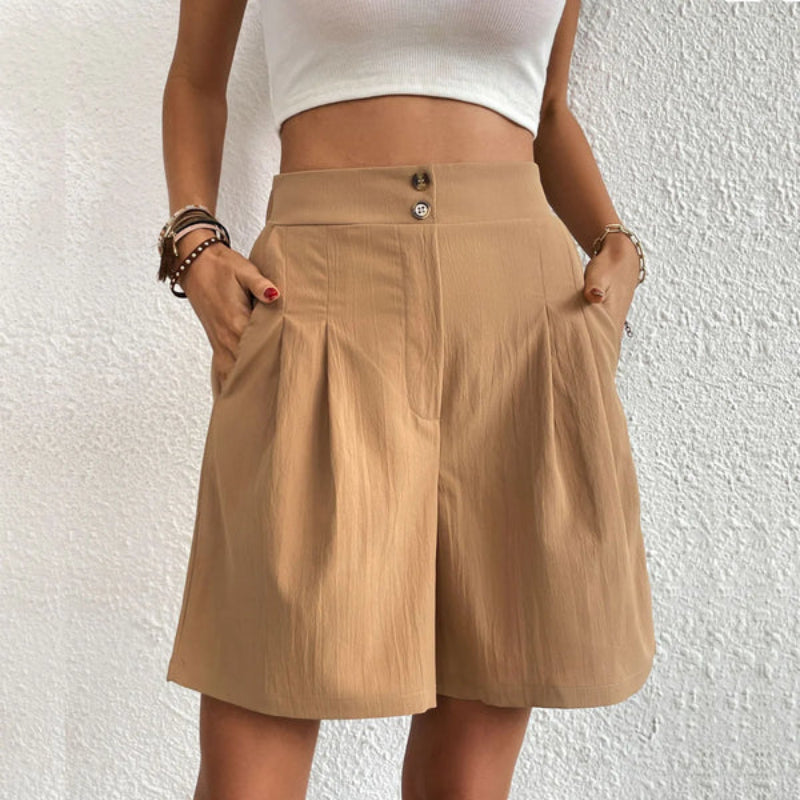 Donna con pantaloncini beige a vita alta, tasche laterali, abbinati a top bianco. Moda estiva casual, abbigliamento femminile trendy.