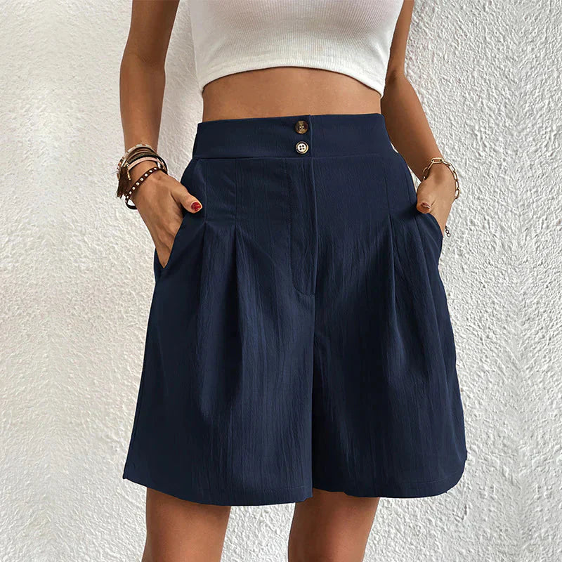 Donna con pantaloncini blu a vita alta, tasche laterali, abbinati a top bianco. Moda estiva casual, abbigliamento femminile elegante.
