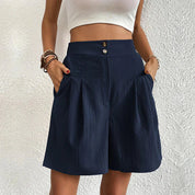 Donna con pantaloncini blu a vita alta, tasche laterali, abbinati a top bianco. Moda estiva casual, abbigliamento femminile elegante.
