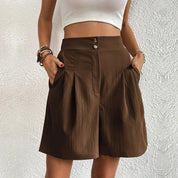 Donna con pantaloncini marroni a vita alta, tasche laterali, bottoni decorativi, abbinati a top bianco. Moda estiva casual, abbigliamento femminile.