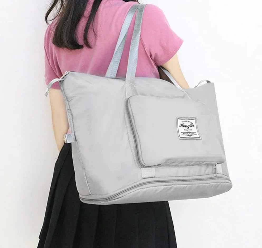 Donna con borsa da viaggio grigia grande, tasca frontale, manici lunghi, indossa maglia rosa e gonna nera. Borsa capiente, moda femminile.