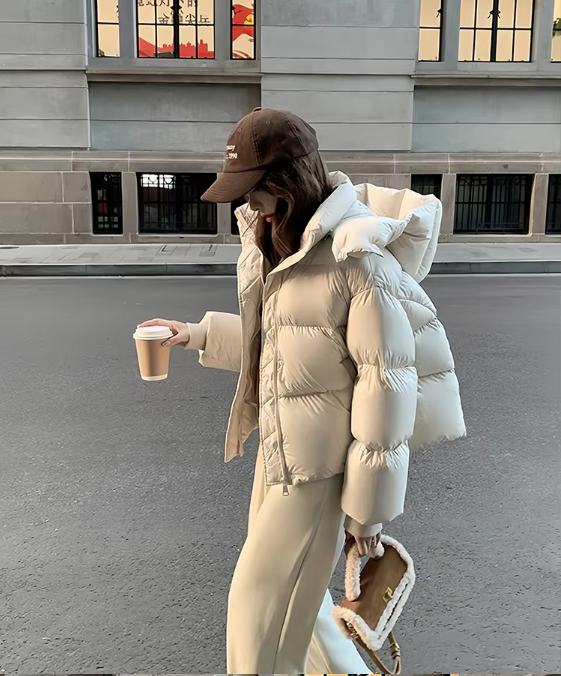 Donna con giacca piumino bianca, cappello marrone, pantaloni beige, tiene caffè e borsa in pelliccia. Moda invernale urbana, abbigliamento casual.