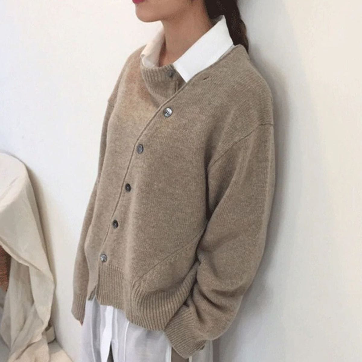 Donna con maglione beige in lana, abbottonato, sopra camicia bianca. Moda autunnale, abbigliamento casual elegante, stile minimalista.