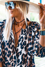 Donna con occhiali da sole e cappello di paglia indossa camicia leopardata. Moda estiva, stile casual chic, accessori eleganti.