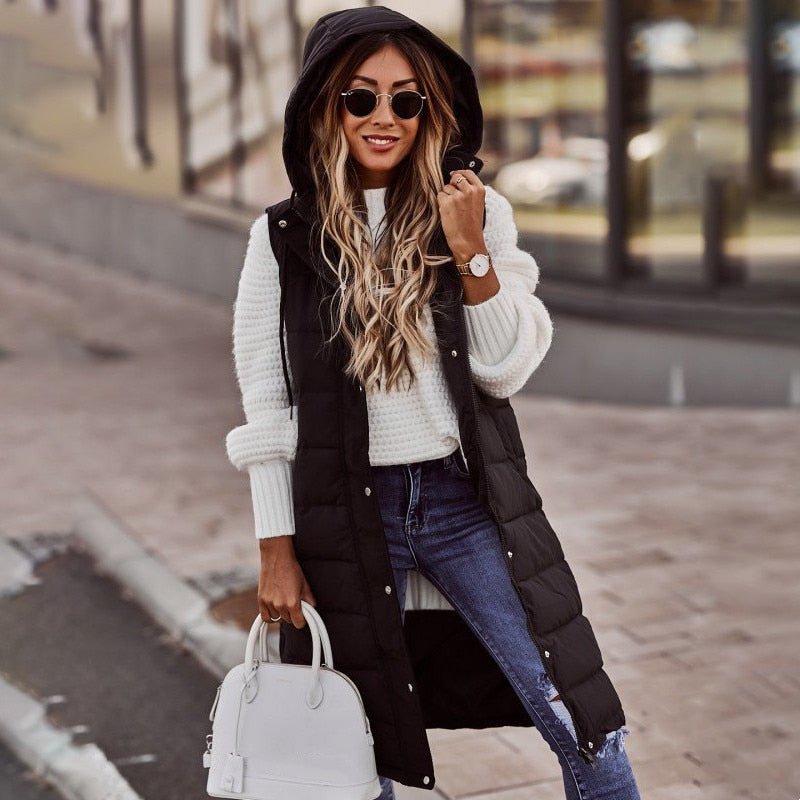 Donna con cappotto lungo nero, maglione bianco, jeans, occhiali da sole e borsa bianca. Moda autunnale, look casual chic.